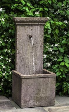 an outdoor fountain with water coming out of it's sides in front of some bushes