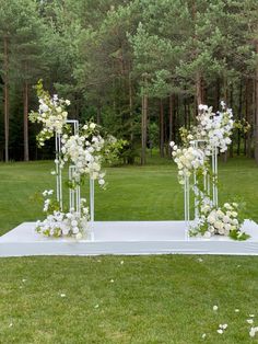 an outdoor ceremony setup with white flowers and greenery on the ground in front of trees