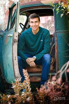 a young man sitting in the back of an old pickup truck smiling at the camera