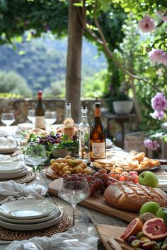 an outdoor table is set with bread, fruit and wine for a picnic or brunch