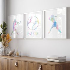 three framed baseball art prints on a wall above a dresser with flowers and candles in vases