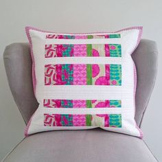 a pink and green pillow sitting on top of a gray chair