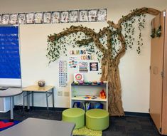 a classroom with desks, chairs and a tree on the wall in front of it