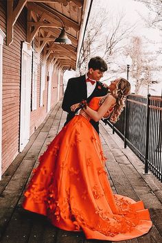 a man in a tuxedo kissing a woman in an orange dress on a porch