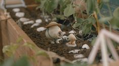 two plants are growing in the soil with little toy figures on them and one is wearing a hat