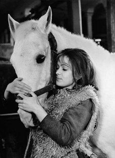 a woman standing next to a white horse