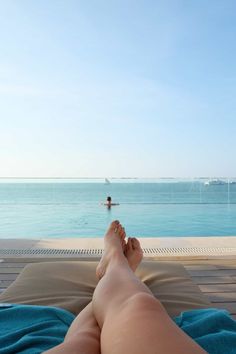 a person laying on top of a blue towel next to the ocean in front of a swimming pool