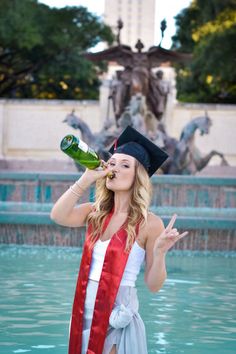 a woman wearing a graduation cap and gown drinking from a bottle in front of a fountain