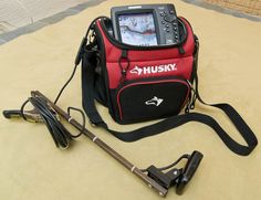 a red and black bag sitting on top of a bed next to a fishing pole