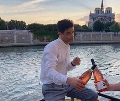 two people on a boat holding bottles of wine and pointing to the camera with an old castle in the background