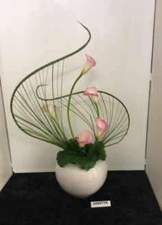 a white vase filled with pink flowers on top of a black table next to a wall