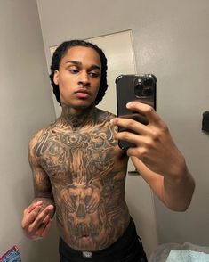 a man with tattoos taking a selfie in front of a mirror while holding a cell phone