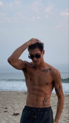 a shirtless man on the beach with his hand in his hair and sunglasses over his head