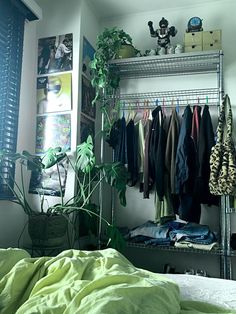 an unmade bed in a bedroom with clothes hanging on the rack and green sheets