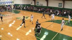 a group of young men playing basketball on a gym court with people watching from the bleachers