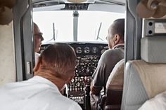 two men sitting in the cockpit of an airplane looking at another man who is standing next to him