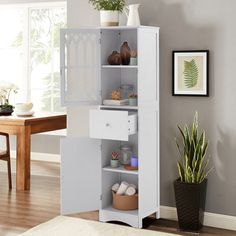 a tall white cabinet sitting in a living room next to a potted plant on top of a wooden table