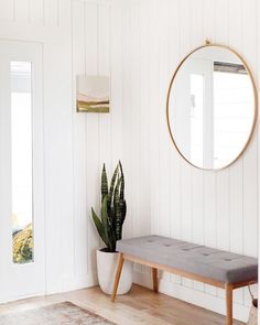 a white room with a bench, mirror and potted plant