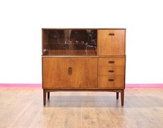 a wooden cabinet sitting on top of a hard wood floor next to a white wall