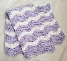 a purple and white crocheted blanket laying on top of a bed next to a pillow