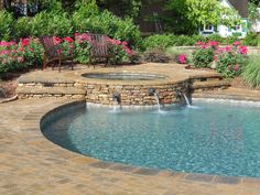 a pool with a waterfall in the middle and chairs around it, surrounded by flowers