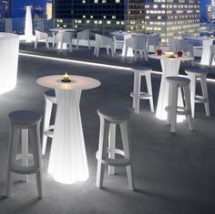 several stools and tables on top of a roof with city lights in the background