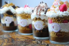 four desserts in small glass containers with toppings on top, sitting on a table