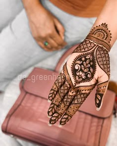 a woman's hand with henna tattoos on it and a purse in the background