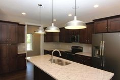 a kitchen with dark wood cabinets and white counter tops, two pendant lights over the sink