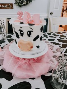 a decorated birthday cake with a cow face on the top and pink tutu skirt