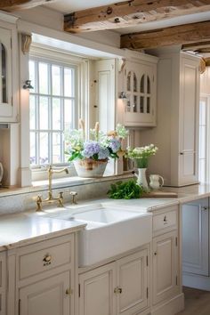 a kitchen with white cabinets and flowers in the window sill on the counter top