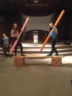 two girls are holding baseball bats while standing on blocks in the middle of a room