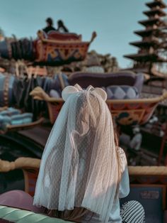 the back of a woman's head with a veil over her head sitting on a bench