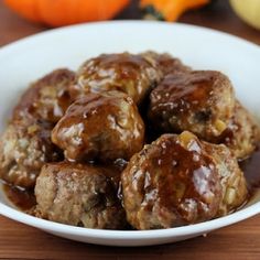 a white bowl filled with meatballs covered in gravy next to mini pumpkins