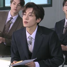 three young men in suits and ties sitting at a table with notebooks on it