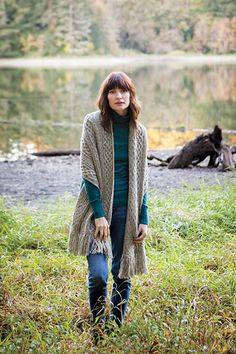 a woman standing in front of a lake wearing a cardigan and holding a purse