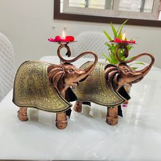 two wooden elephants holding candles on top of a white table with flowers in the background