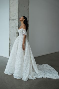 a woman in a white wedding dress standing against a concrete wall and looking up at the sky