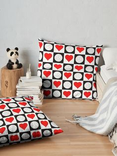 two pillows with red and black hearts on them sitting on a wooden floor next to a stack of books