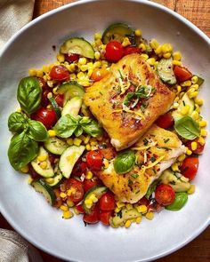 a white bowl filled with fish, corn and veggies on top of a wooden table