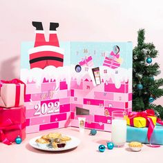 a table topped with presents next to a christmas tree and pink wallpapered calendar