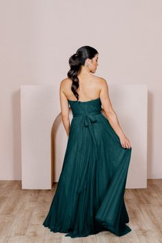 a woman in a green dress standing on a wooden floor with her back to the camera