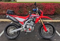 a red dirt bike parked in a parking lot next to bushes and shrubbery,