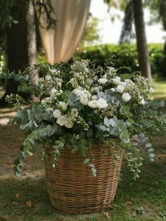 a basket filled with white flowers sitting on top of a grass covered field next to trees