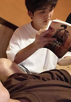 a young man reading a book while sitting on a bed