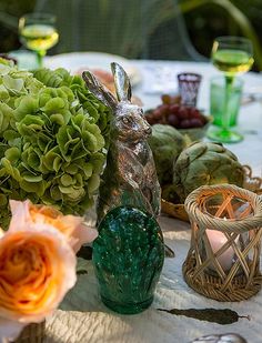 a table topped with green vases filled with flowers and greenery next to a rabbit figurine