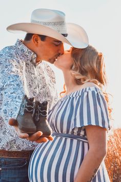 a pregnant woman kissing a man wearing a cowboy hat and holding a pair of boots