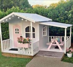 a small pink and white house with flowers on the porch