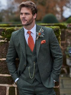 a man in a suit and tie standing next to a brick wall with moss growing on it