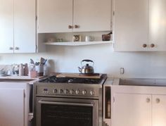 a stove top oven sitting inside of a kitchen next to white cupboards and drawers